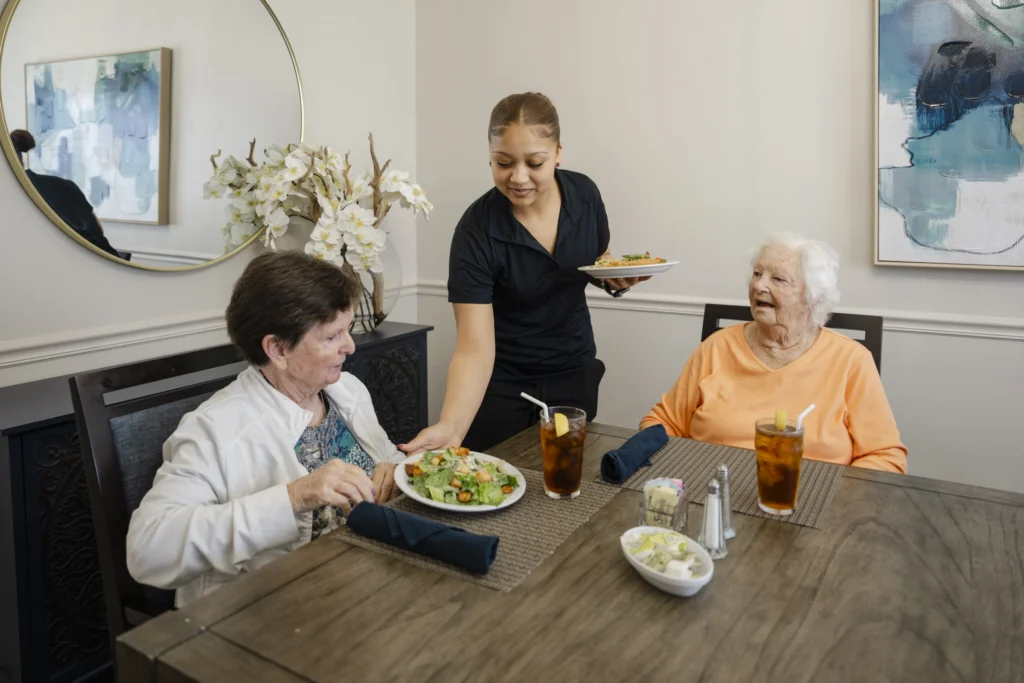 Server placing salad on table for two residents